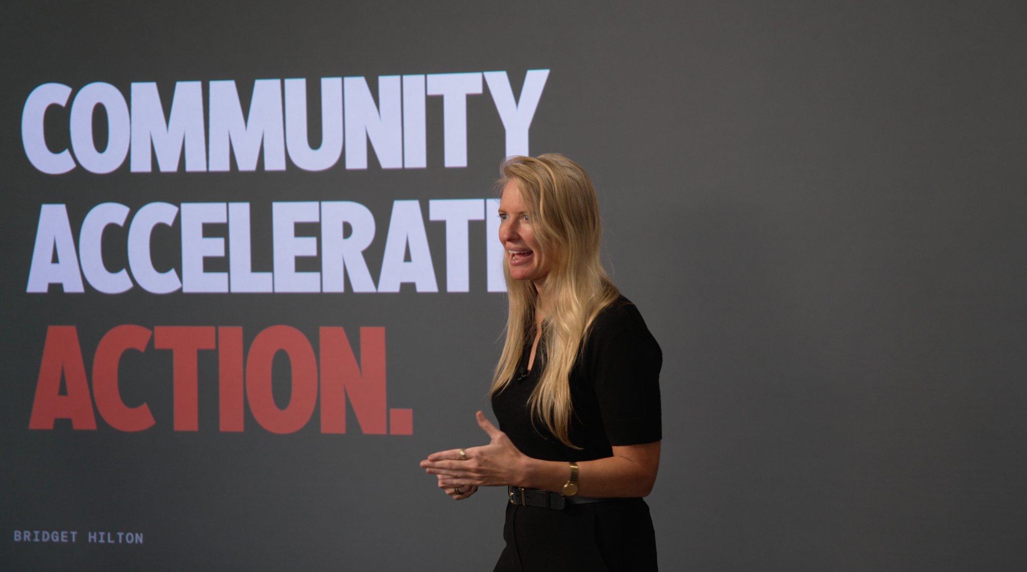 Bridget Hilton on stage in front of a Community Accelerates Action slide