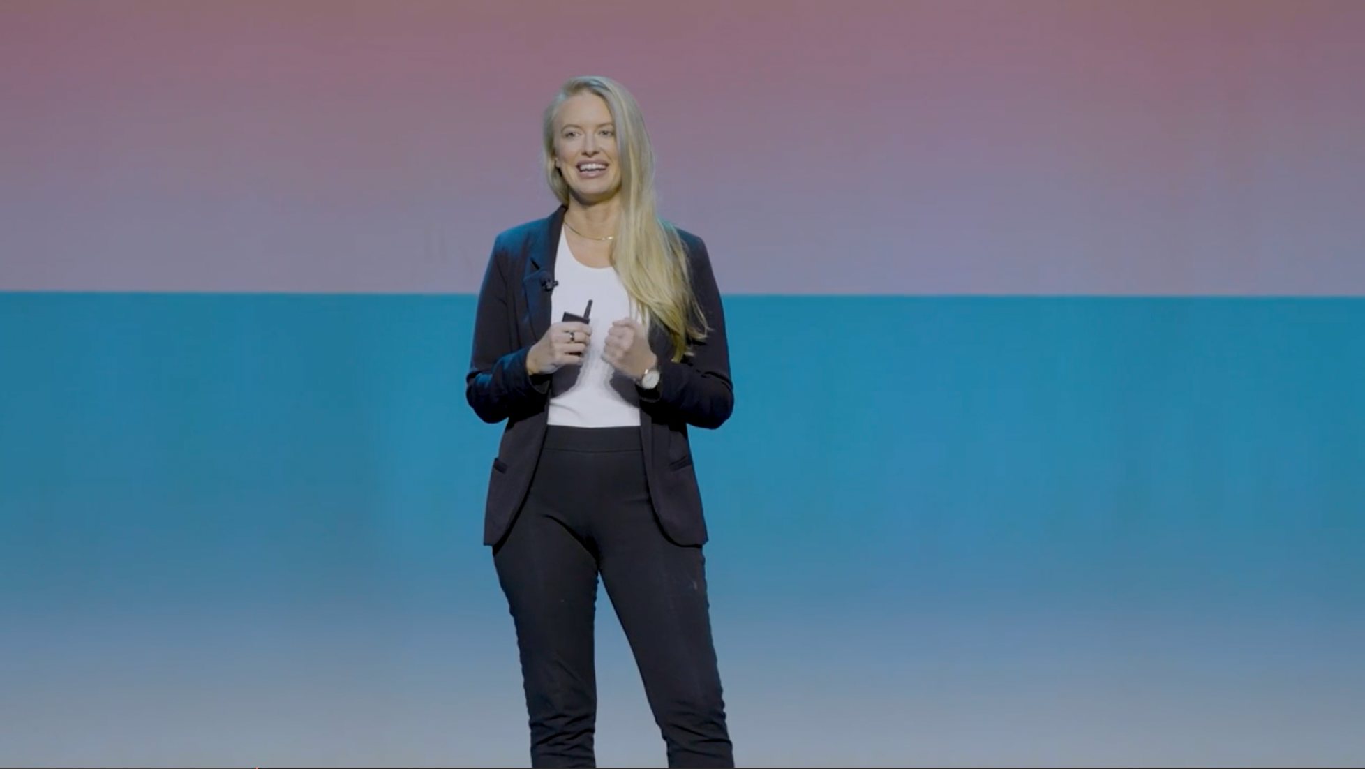 Bridget Hilton speaking on stage in front of a pink and blue backdrop