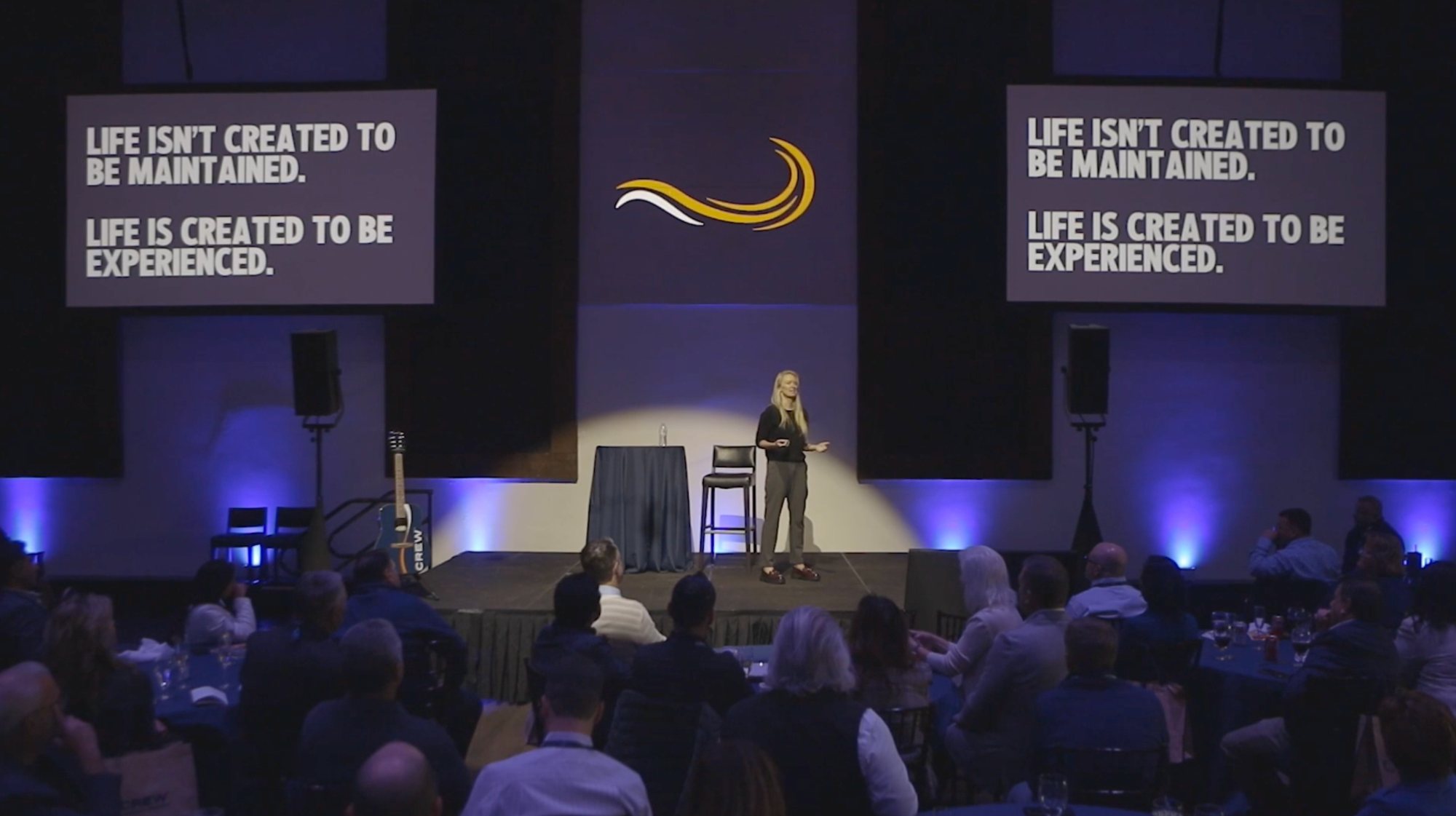 Bridget speaking at the CREW conference in a spotlight between two screens